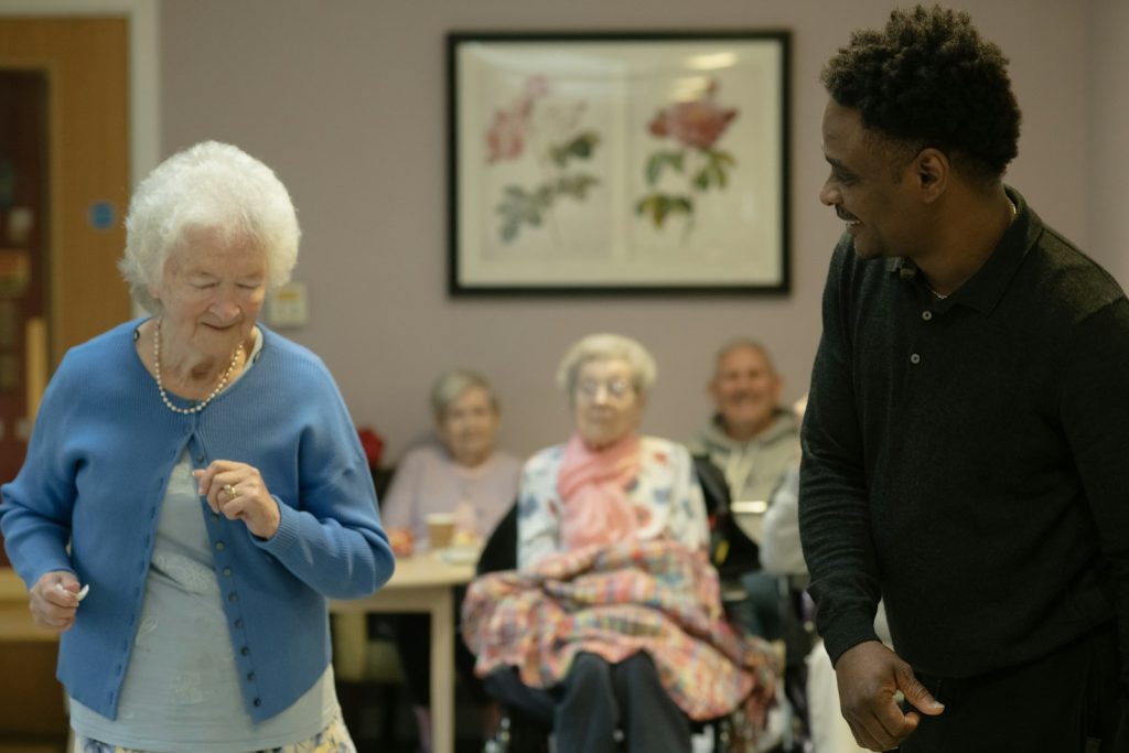 Een vrijwilliger danst vrolijk met een oudere bewoonster